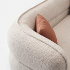 Lune Bouclé Crescent Sofa detail with cream textured upholstery and warm accent pillow